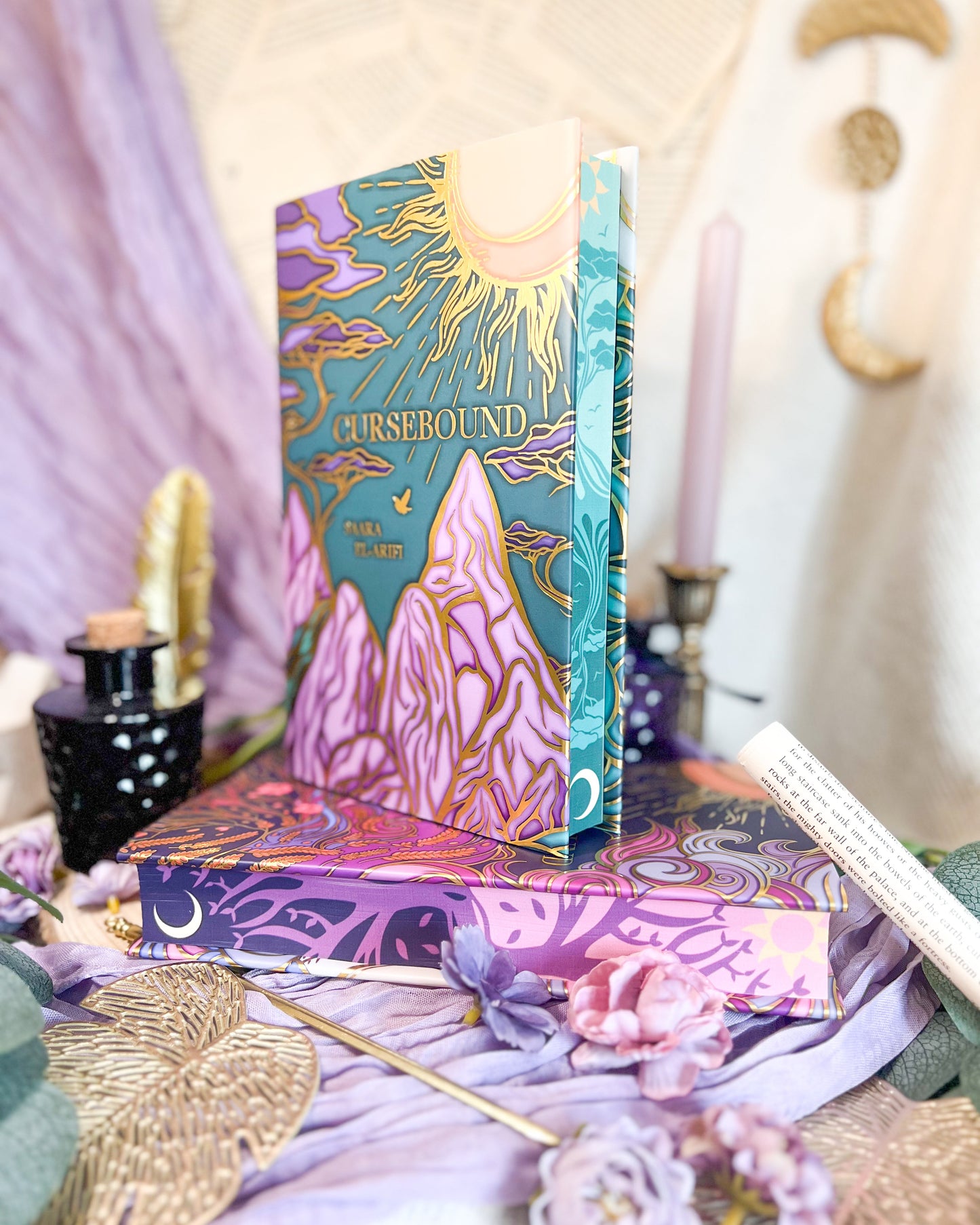 Book titled 'Cursebound' on top of "Faebound" book with decorative covers on a table with flowers and candles.