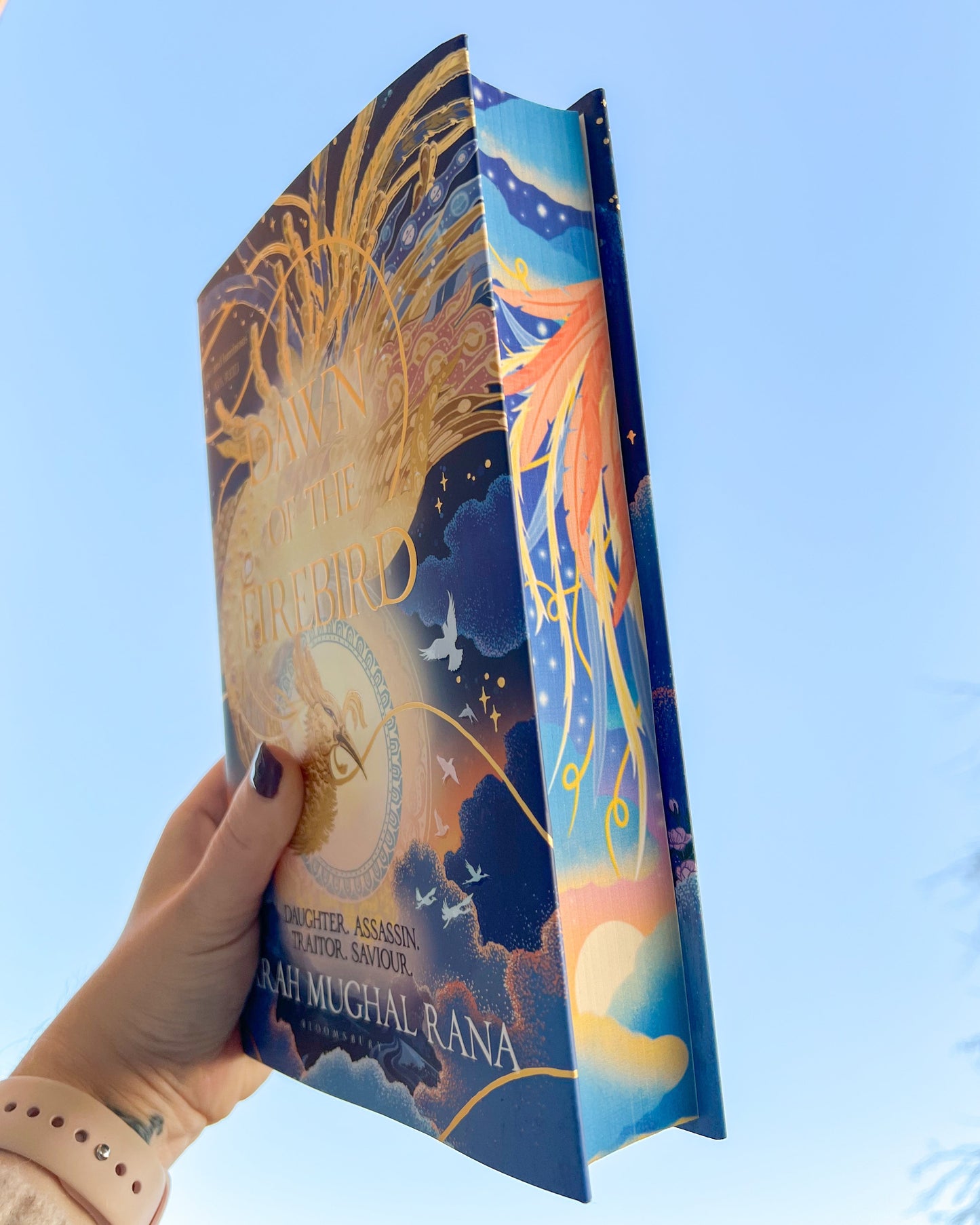Book with colorful cover held against a clear blue sky