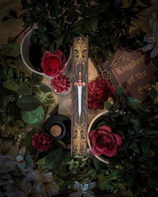 Decorative dagger book edge design with gold embellishments on a bed of flowers and leaves