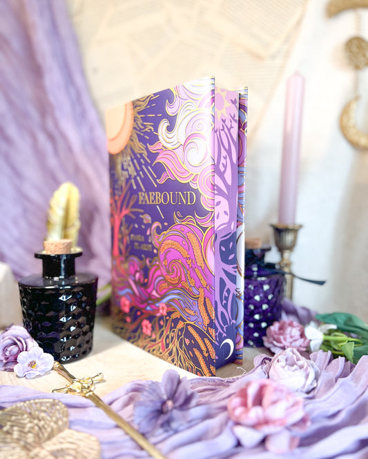 Lilac and gold decorative book with floral design on a table with flowers and a candle.